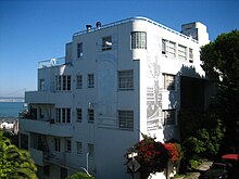 A white and silver building built with curved corners and streamlined features, stepped back along the slope of a hill.