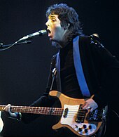 Coloured image of a long-haired McCartney in the 1970s playing a guitar.