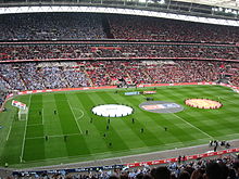 A full football stadium, with spectators in the left half wearing blue, and those in the right half wearing red